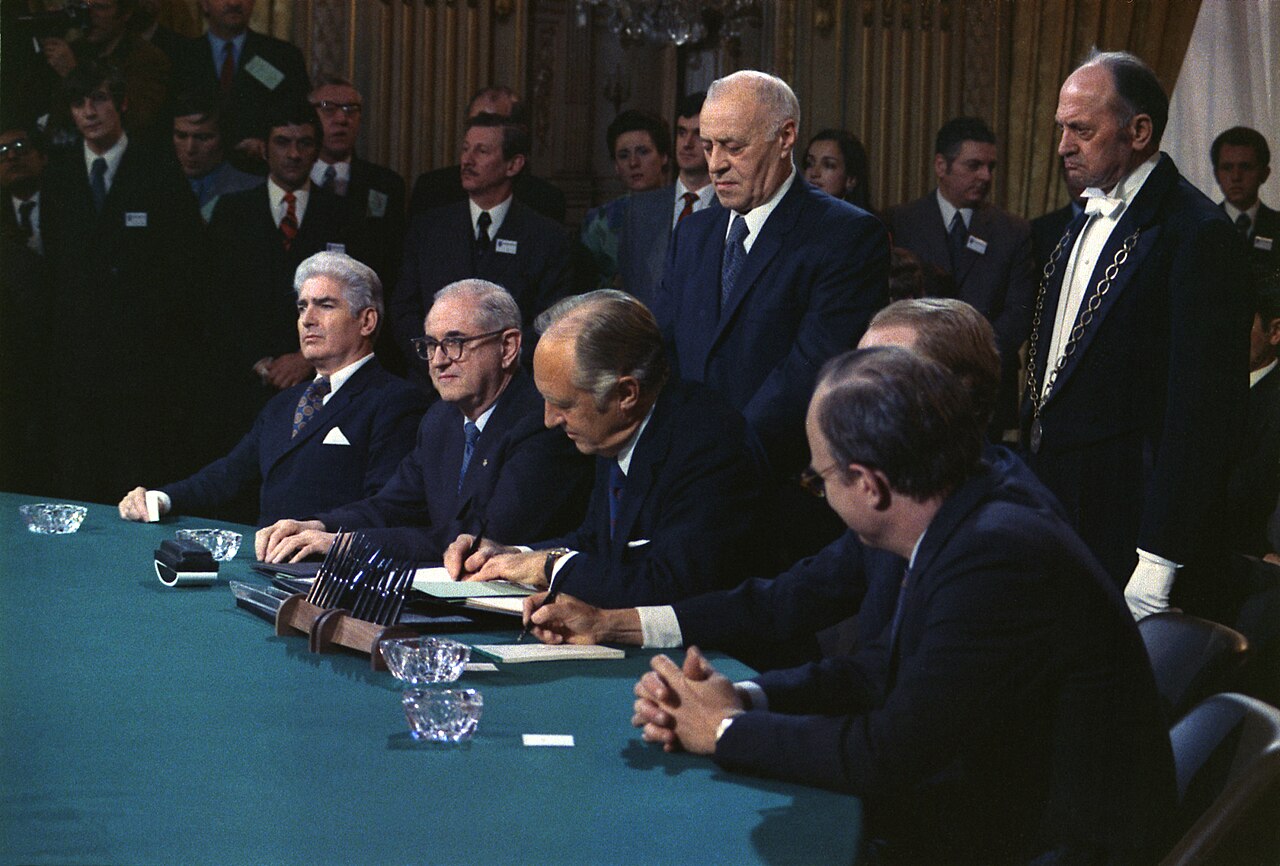 Diplomats sit around a table as U.S. Secretary of State William Rogers signs the Paris Peace Accords