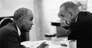 Roy Wilkins and President Lyndon Johnson lean toward each other talking
