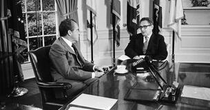 President Richard Nixon and Henry Kissinger talking at the Resolute Desk in the Oval Office.
