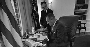 LBJ sitting at a desk with White House aide Walter W. Jenkins standing behind him 