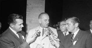 LBJ talking to reporters holding microphones