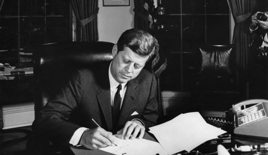 John Kennedy sitting at his desk writing