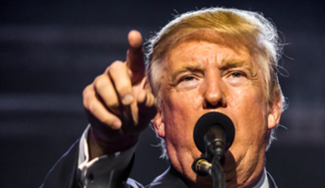 Donald Trump behind a mic pointing