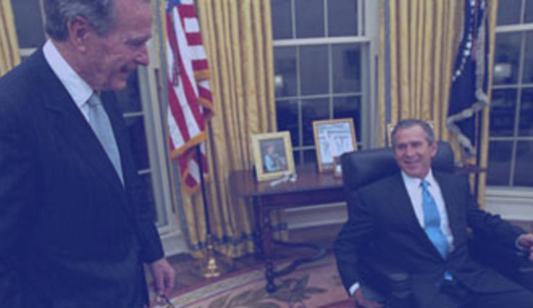 Bush 43 sits at the desk in the Oval Office for the first time, as his father looks on