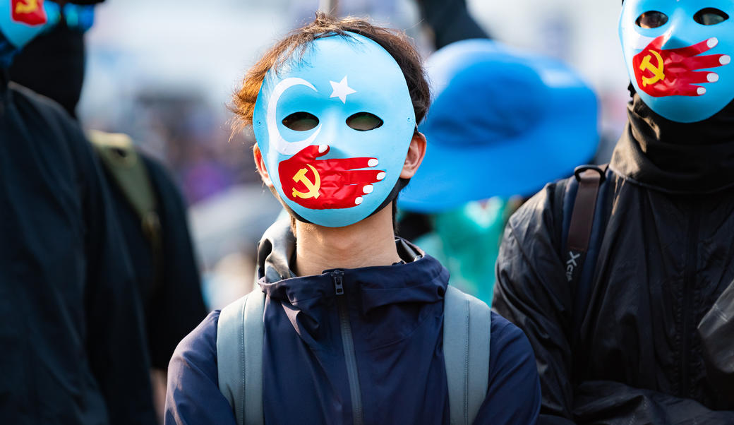 Hong Kong protestors wear masks symbolizing the Communist Party of China's silencing of Uyghur Muslims at a solidarity rally