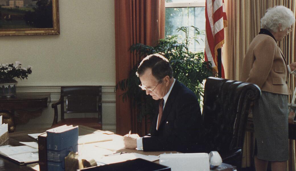 George H. W. Bush sitting at his desk with Barbara Bush behind him