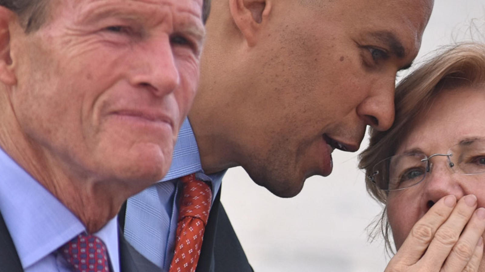Corey Booker whispers to Elizabeth Warren; Senator Blumenthal in the foreground